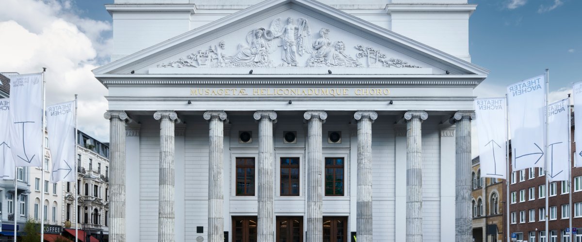 Theater Aachen Frontale Ansicht des Theaters Aachen mit seinen Säulen vor einem blauen Himmel mit zarten Wolken.