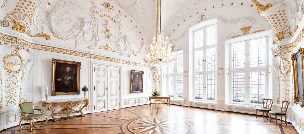 Weißer Saal mit Stuck und Gold an der Decke. Foto einer Ecke des Saals mit tollem Parkett.