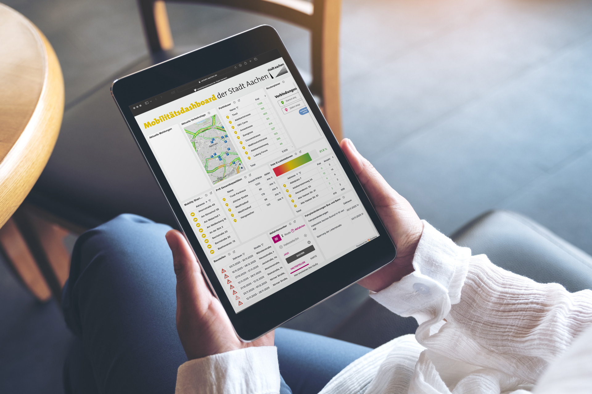 Frau im Schneidersitz sitzt, haält ein Tablet mit dem Mobilitätsdashboard der Stadt Aachen.