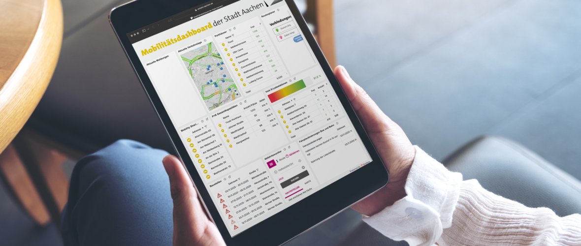Mobilitätsdashboard Frau im Schneidersitz sitzt, haält ein Tablet mit dem Mobilitätsdashboard der Stadt Aachen.