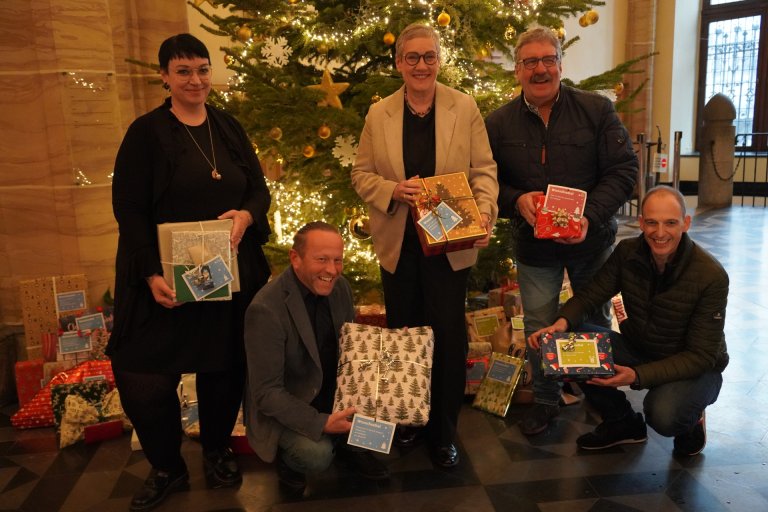 Personen vor Weihnachtsbaum im Rathaus halten Geschenke in der Hand