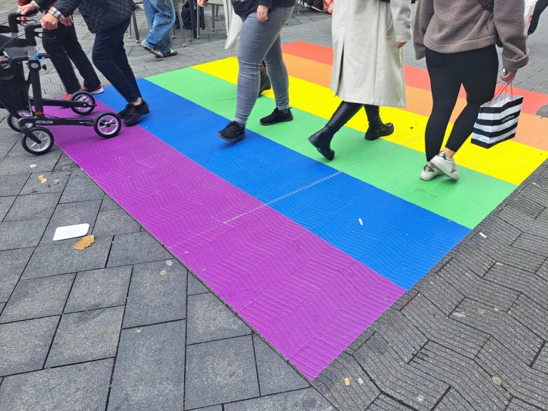 Regenbogen-„Zebrastreifen“ in der Adalbertstraße Mehrfarbige Streifen auf Straßenbelag in einer Fußgängerzone. Vereinzelte Menschen laufen über die bunte Fläche