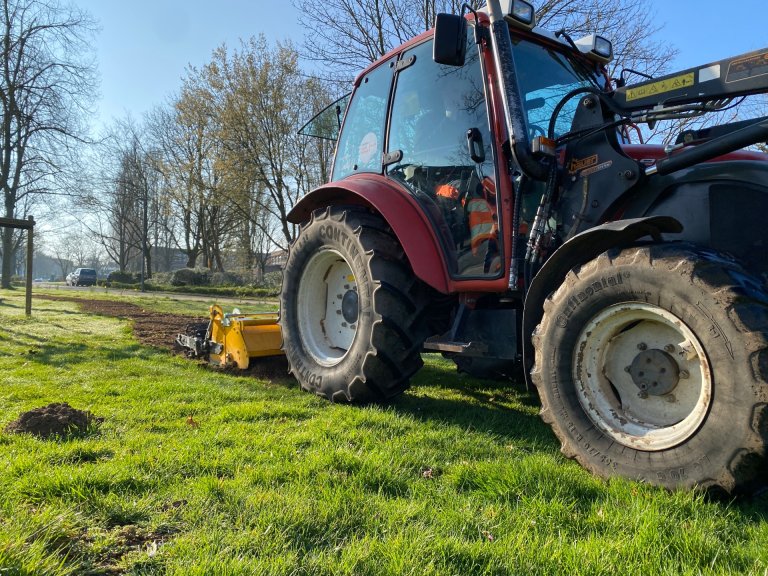 Ein Traktor zieht mit einem gelben Aufsatz Furchen in den Boden