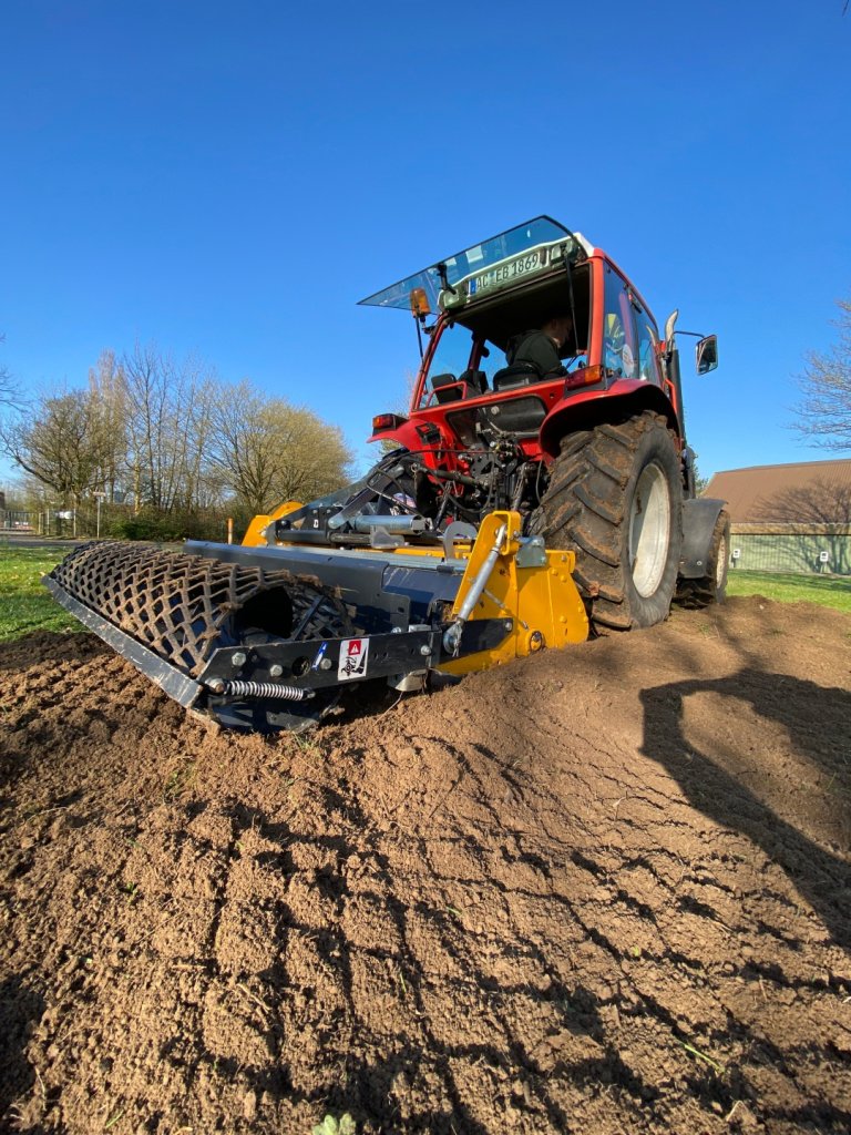 Ein Traktor zieht mit einem gelben Aufsatz Furchen in den Boden
