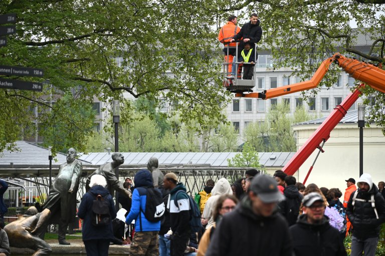 Drei Personen stehen in einem Korb einer Hubarbeitsbühne. Darunter viele Menschen. Im Hintergrund Elisenbrunnen und Bäume.