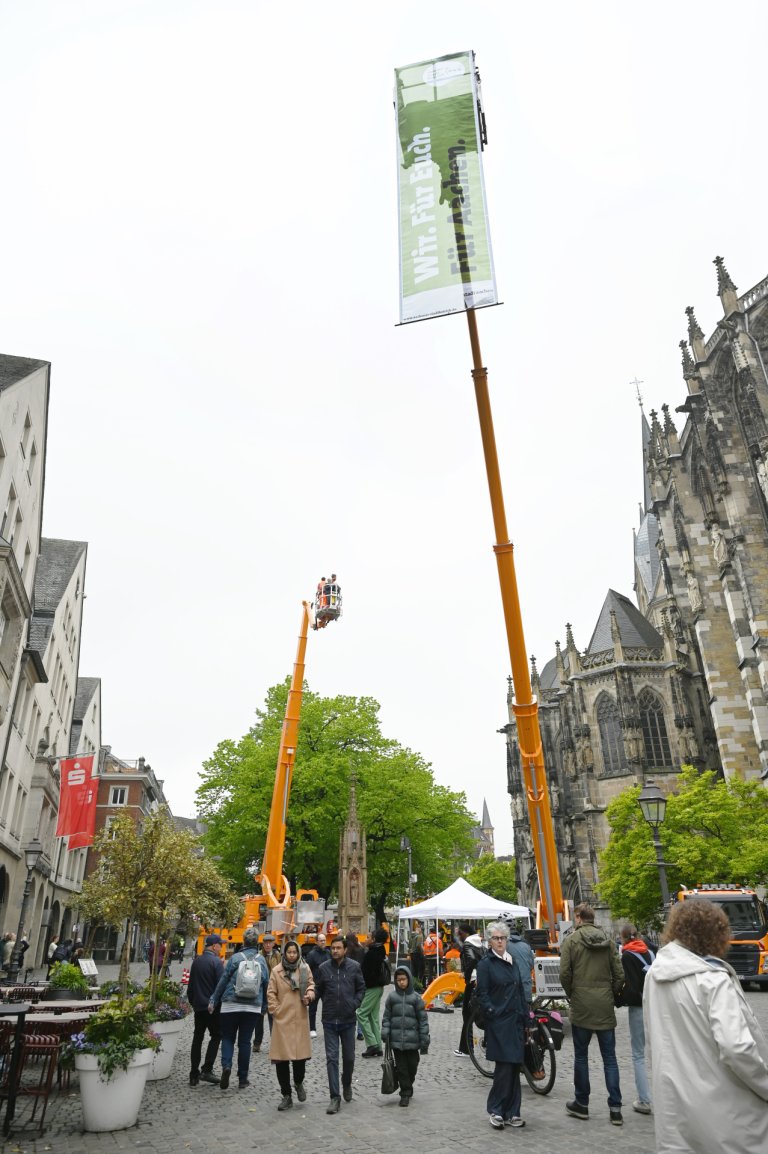 Zwei ausgefahrene Hubarbeitsbühnen vor dem Aachener Dom. An der rechten Hubarbeitsbühne hängt ein grünes Banner mit Schrift "Wir. Für Euch. Für Aachen."