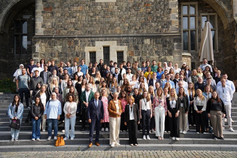 Eine große Gruppe Menschen steht auf einer Treppe. Im Hintergrund die Rückseite des Aachener Rathauses.