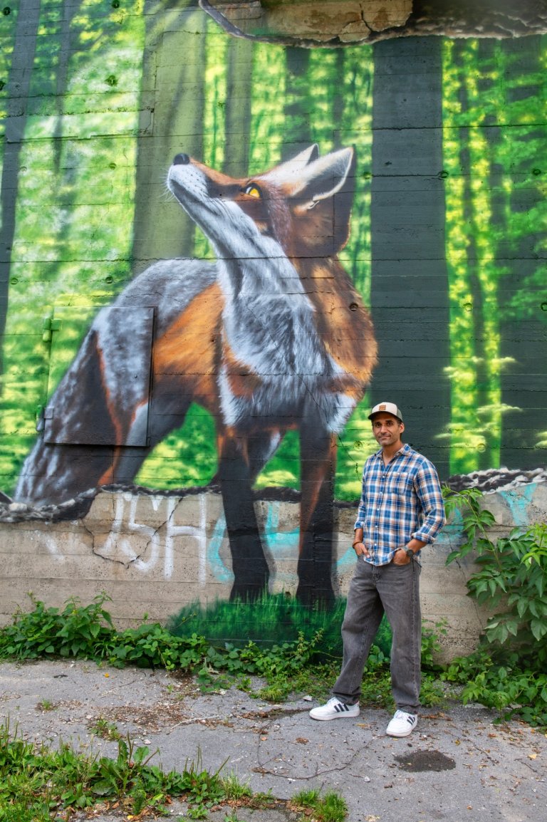 Ein Mann steht vor einer Wand, auf die ein Fuchs gesprayed ist.