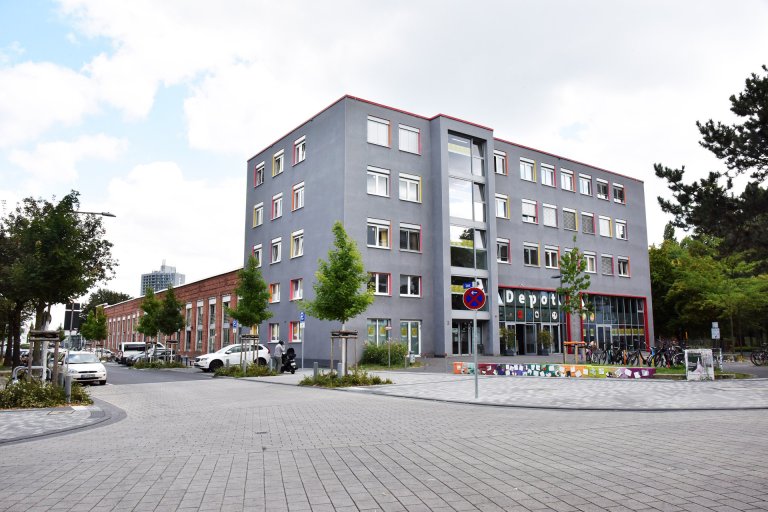 Ein viergeschössiger Kopfbau, grau gestrichen mit großer Fensterfront