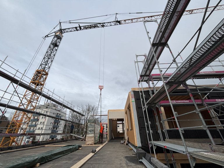 Ein Kran lädt verpackte Fenster auf dem Dach eines Gebäudes auf einer Baustelle ab.