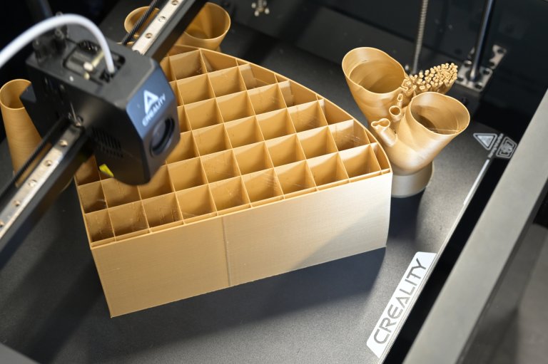 Aufsicht auf einen 3D Drucker, der eine Form aus goldenem Material erstellt.