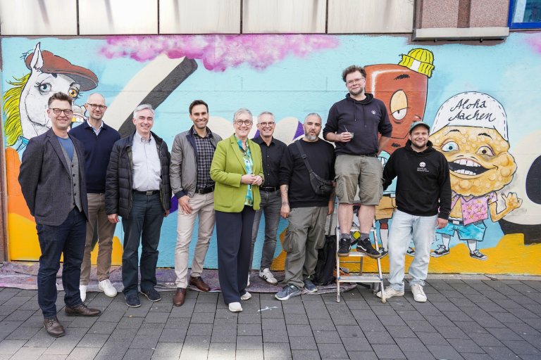 v.l.n.r.: Kai Hennes (Citymanagement), Dr. Kevin Meyer (Midstad), Dirk Kuckelkorn, Gregory Hedderich (Isa Adalbertstraße), Oberbürgermeisterin Sibylle Keupen, Guido Kuckelkorn (ISA Adalbertstraße), die Künstler Michael Gerst, Alex Elsen, Paul Sous
Händler, Künstler und Oberbürgermeisterin vor einer Streetart-Fassade