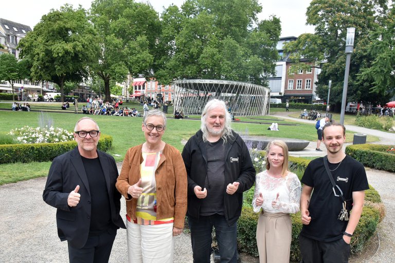 Fünf Menschen stehen in einem Park, lächeln in die Kamera und heben den Daumen.