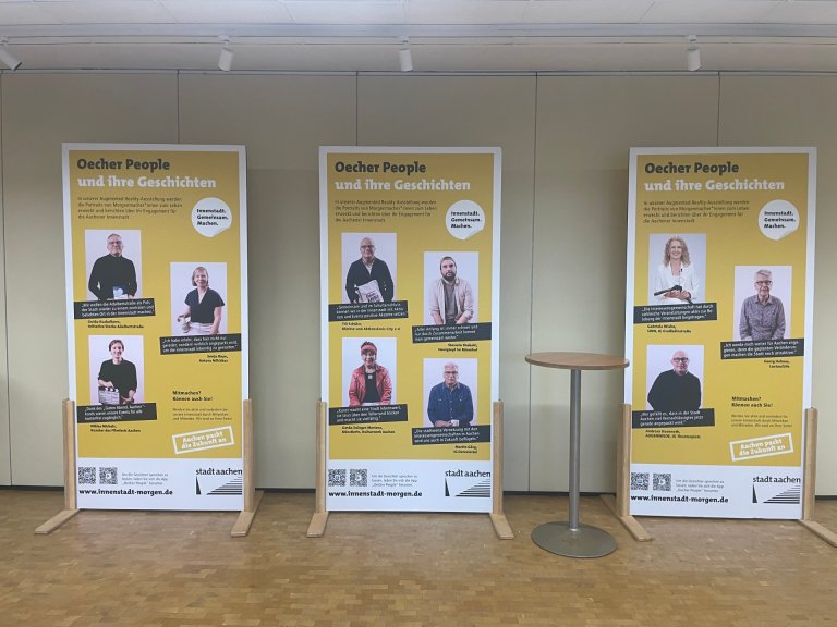 Vier Aufsteller mit Menschen drauf stehen vor einer Wand