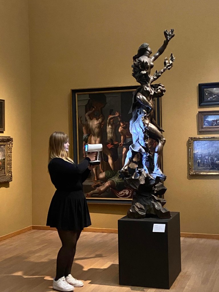 Eine junge Frau scannt mit einem technischen Gerät eine graue Skultptur im Museum.