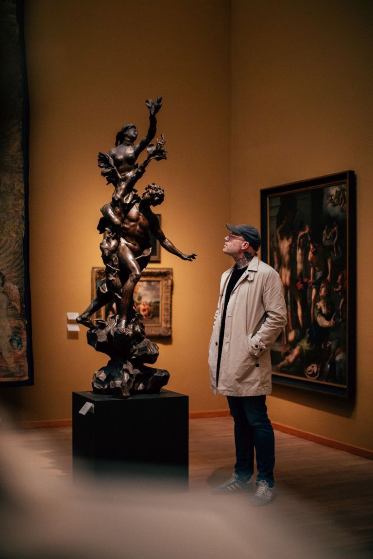 Ein Mann mit Kappe und Brille schaut eine bronzen-graue Skulptur im Museum an.