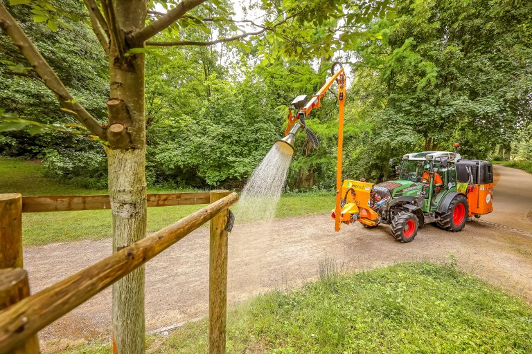 Ein Baum wird von einem Gießfahrzeug gegossen.
