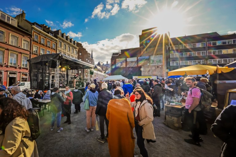 Viele Menschen stehen auf einem Platz. Vorne auf einer Bühne singt eine Person in ein Mikro. Im Hintergrund sind der Dom und die Aachener Altstadt zu sehen.