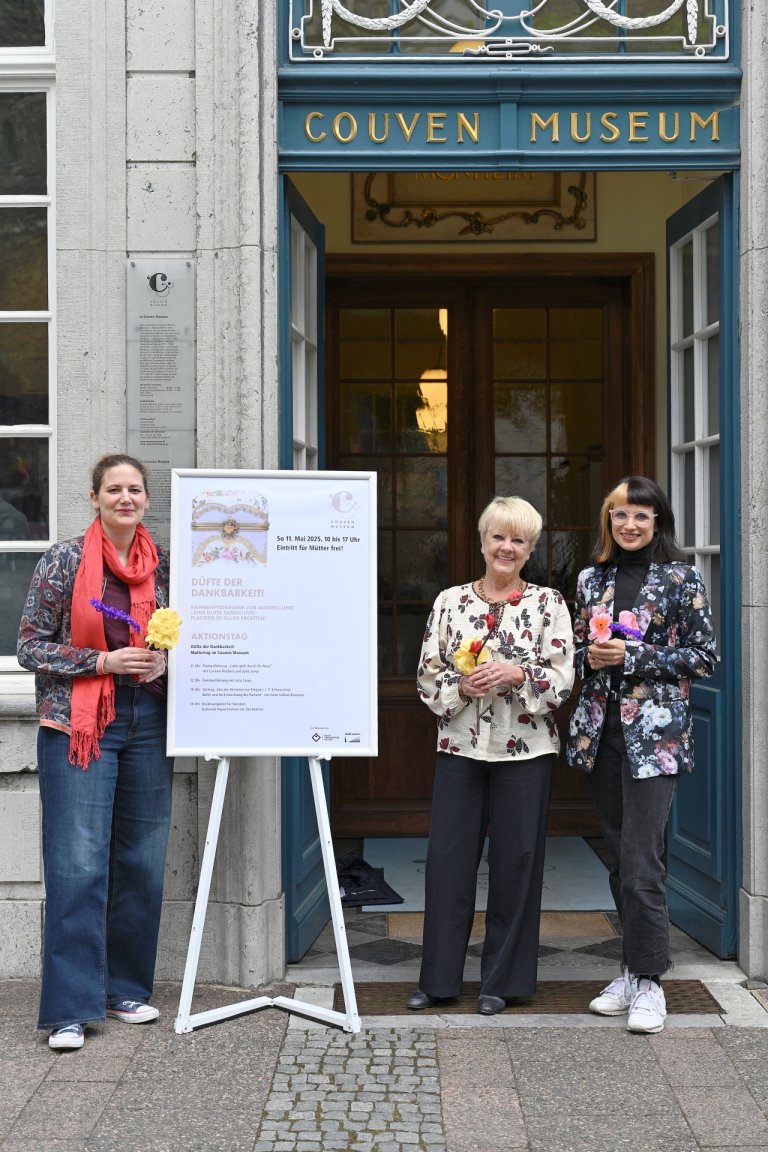 Drei Frauen stehen vor dem Couven Museum und halten Papierblumen in der Hand.