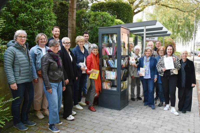 Eine Gruppe von Menschen steht neben einem Glaskasten mit Büchern.