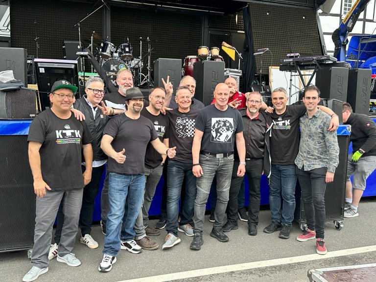 Eine große Gruppe männlicher Musiker vor einer Bühne stehend. 