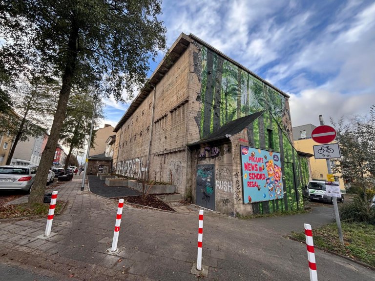 Ein Hochbunker: die vordere Fassade ist mit einer Wald-Streetart verschönert, an der linken Fassade sind angelegte Beete zu sehen.
