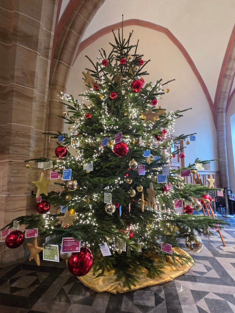 Ein rot-gold geschmückter Weihnachtsbaum im Foyer des Aachener Rathauses, der zusätzlich mit Wunschzettelkarten behangen ist.