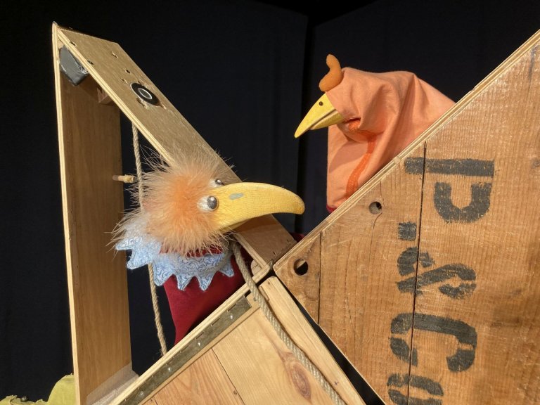 Zwei Handpuppen schauen sich durch ein Holzgestell hindurch an.