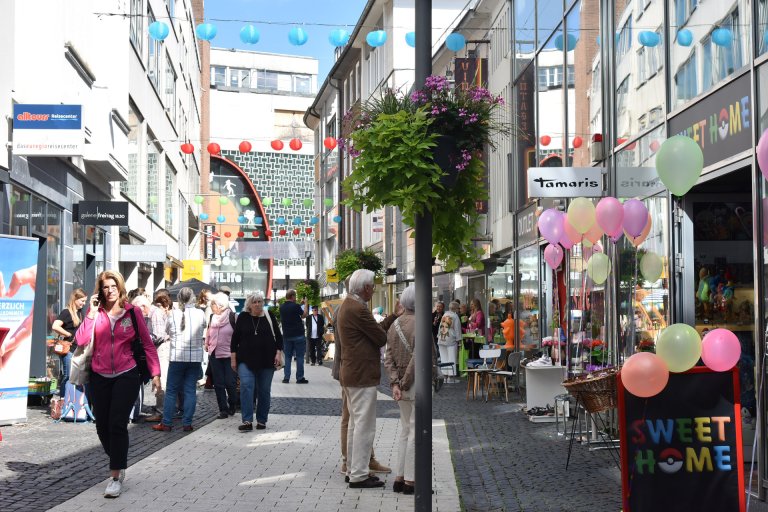 Eine Einkaufsstraße mit vielen Passanten und bunten Lampions, die über der Straße gespannt sind.