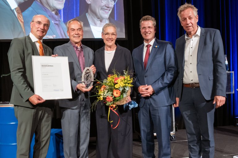 Der Preisträger des Aachener Ingenieurpreises mit einer Gruppe, die ihm den Preis überreicht haben, auf der Bühne im Aachener Krönungssaal mit der Trophäe des Preises, einer Urkunde und einem Blumenstrauß in den Händen.