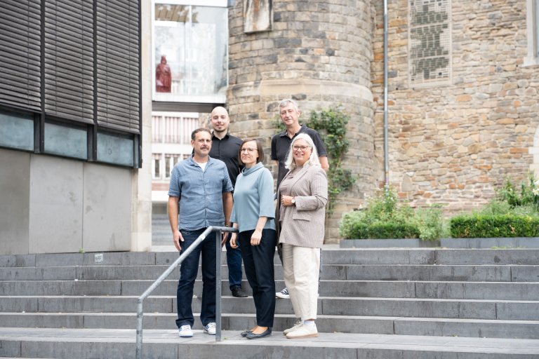 5 Menschen stehen auf einer Treppe. Im Hintergrund der Durchgang zwischen Rathaus und Verwaltungsgebäude Katschhof zum Aachener Markt.