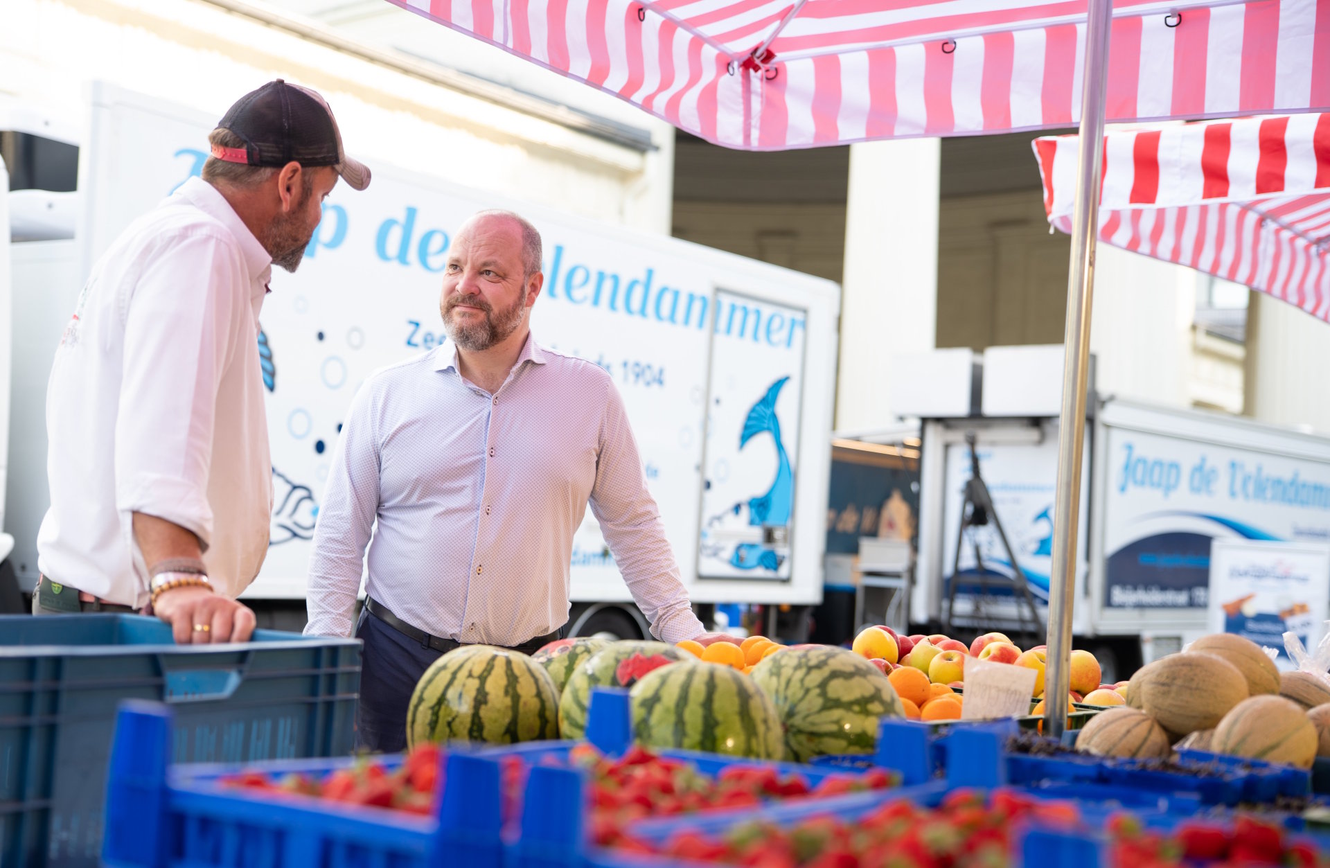 Zwei Männer unterhalten sich an einem Marktstand.