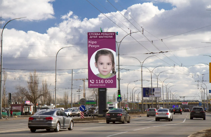 Eine große Anzeigetafeln mit einem Foto eines Kinders und einer Telefonnummer auf einer Hauptstraße in einer Stadt.