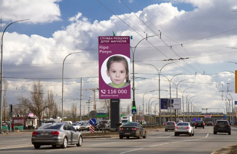 Eine große Anzeigetafeln mit einem Foto eines Kinders und einer Telefonnummer auf einer Hauptstraße in einer Stadt.