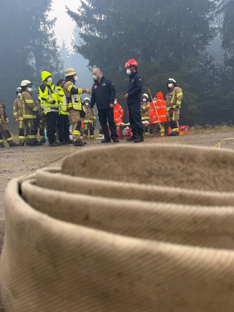 Mehrere Feuerwehrleute und Oberbürgermeister Michael Ziemons stehen in einem Waldstück im Hohen Venn. Im Vordergrund ist ein großer Löschschlauch zu sehen.