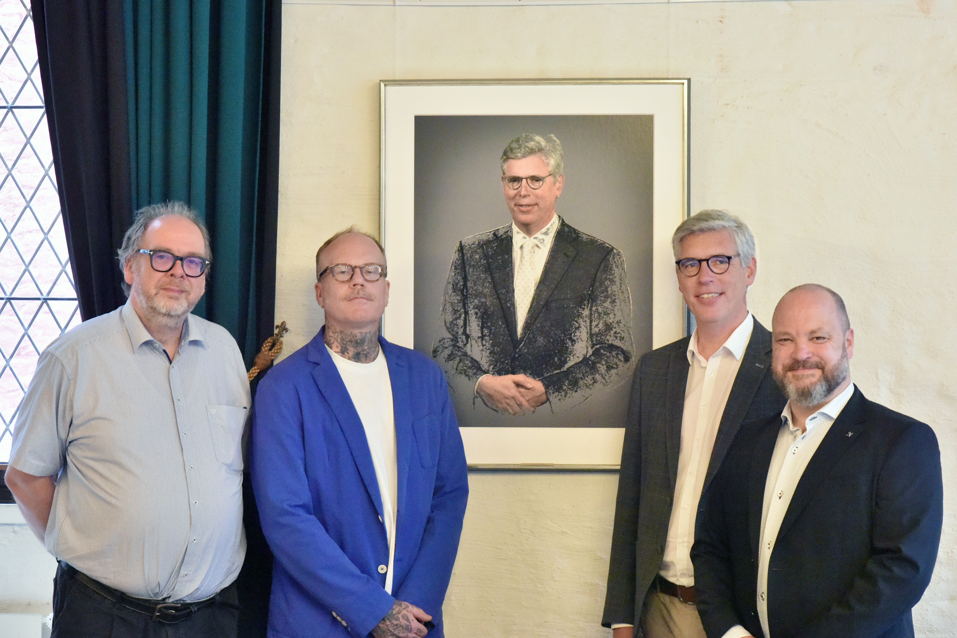 Vier Männer stehen vor einem Portrait des Oberbürgermeisters a.D. Marcel Philipp.