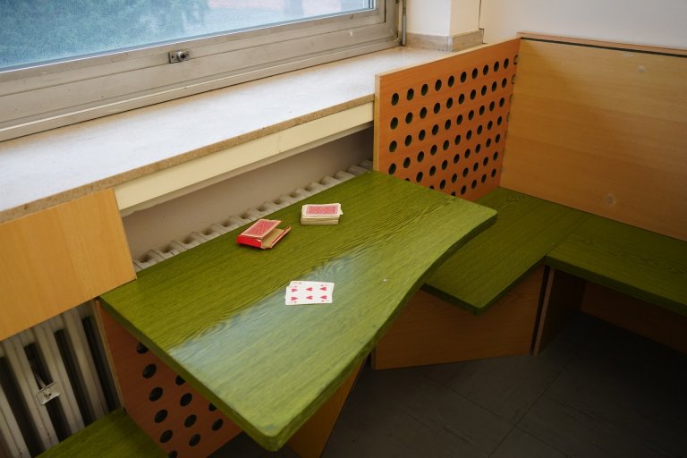 Eine grün-hölzerne Sitzecke mit einem Tisch, auf dem Spielkarten liegen. 