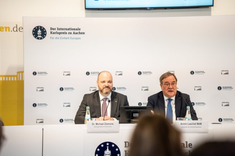 Zwei Männer sitzen nebeneinander auf einem Podium.