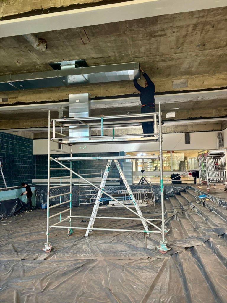 Ein Handwerker steht auf einem Gerüst in einem leeren Schwimmbecken.