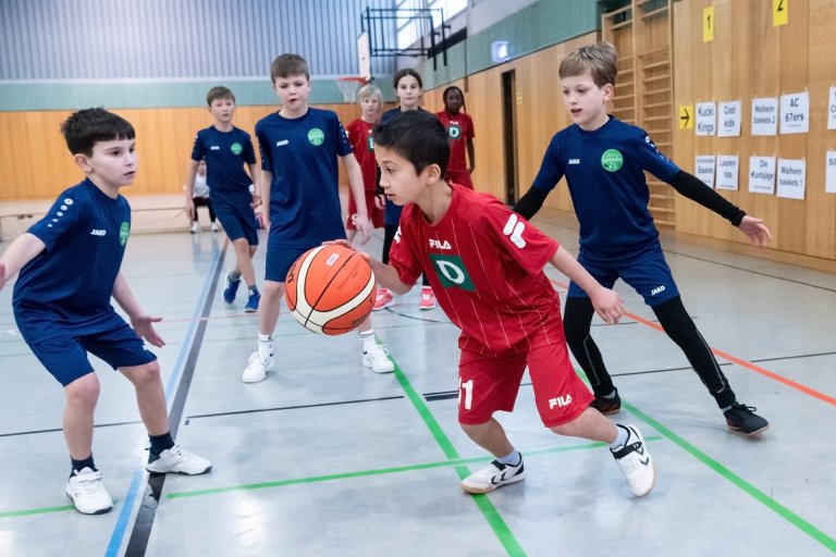 Eine Gruppe von Kindern spielt in einer Sporthalle Basketball