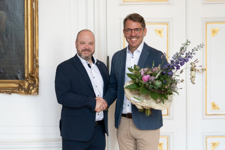 Ein Mann reicht einem anderen Mann, der einen Blumenstrauß trägt, die Hand.