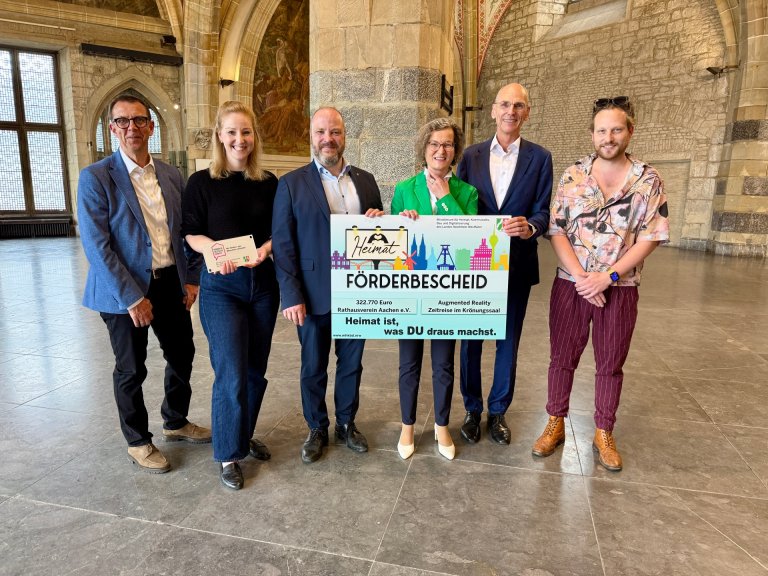 Sechs Personen stehen im Aachener Krönungssaal und halten einen großen Fördermittelbescheid in den Händen.