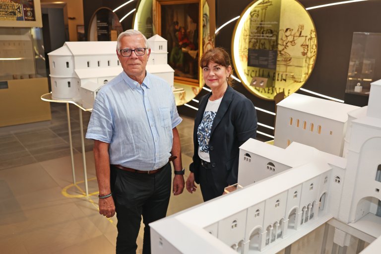Zwei Personen stehen in einem Museum hinter weißen Gebäudemodellen.