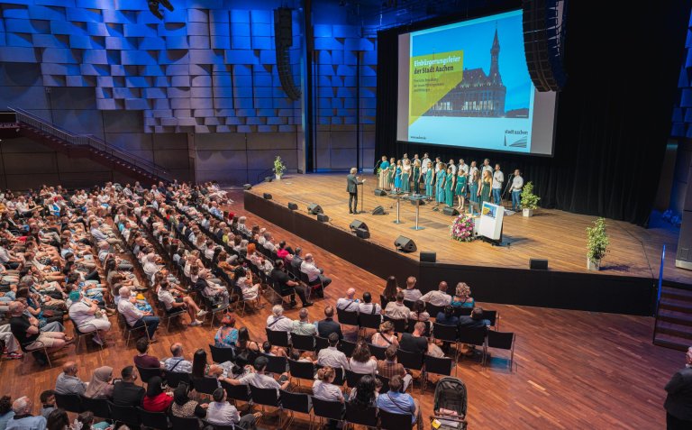 Ein Chor singt auf einer großen Bühne vor hunderten Menschen im Saal