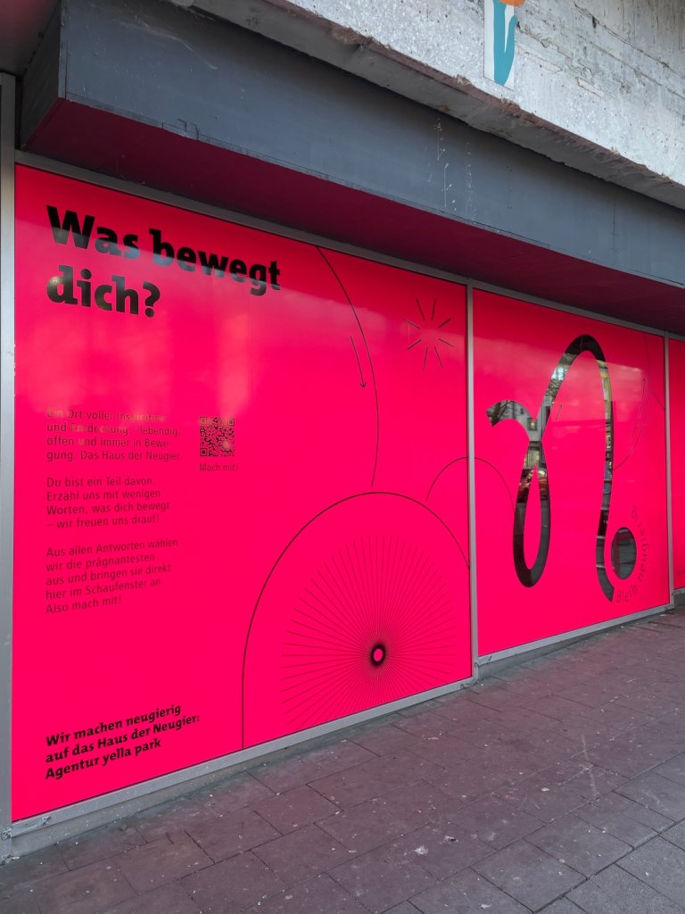 Eine beklebte Schaufensterfläche in Pink mit vielen Freiformen und der Frage "Was bewegt dich".