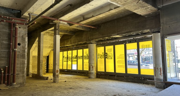 Der Innenraum einer Baustelle mit Blick auf ein Schaufenster, das mit einer gelben Schaufensterbeklebung zu sehen ist. 