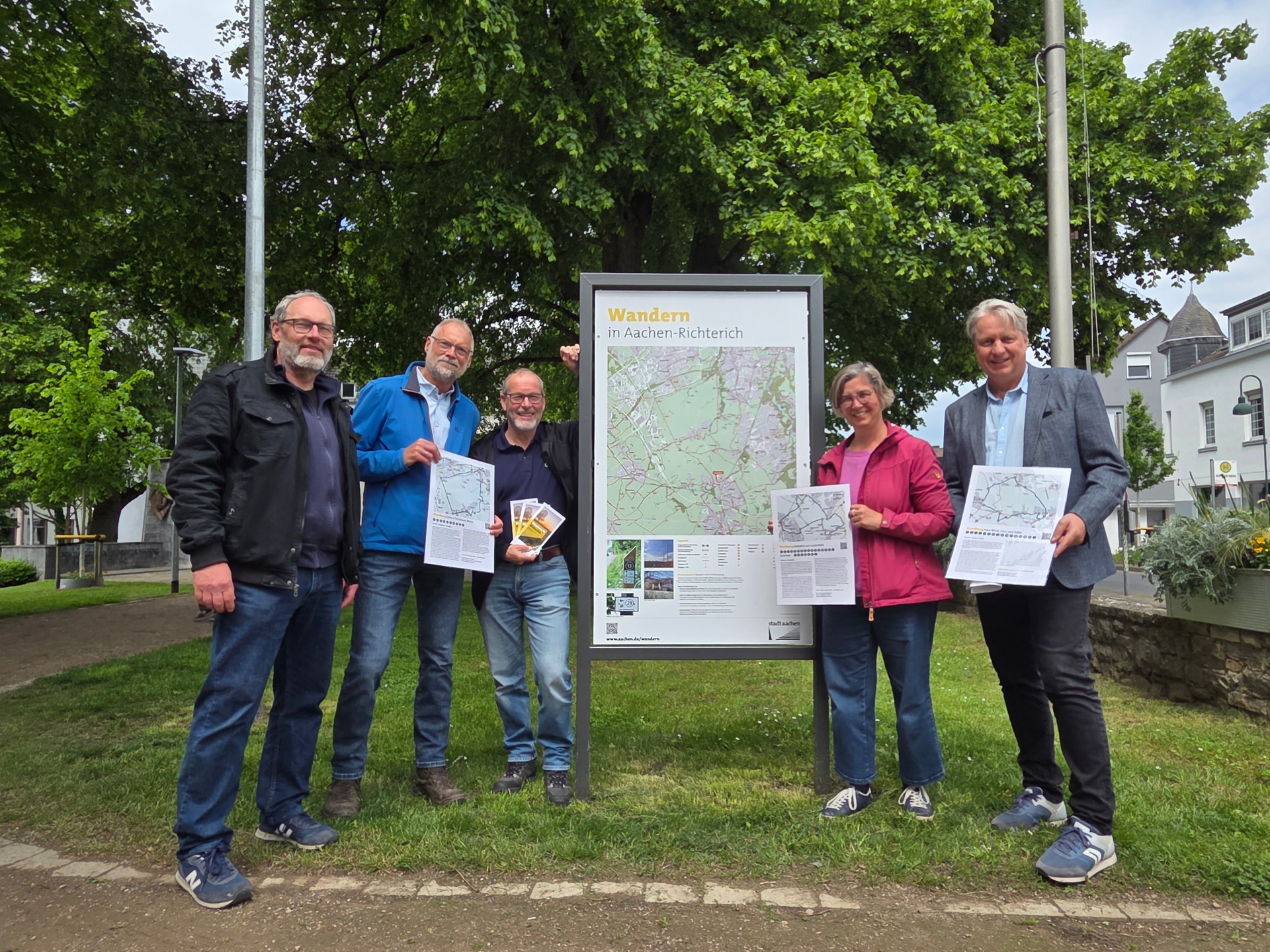 Eine Gruppe steht links und rechts neben einer Wanderorientierungstafel in Richterich.
