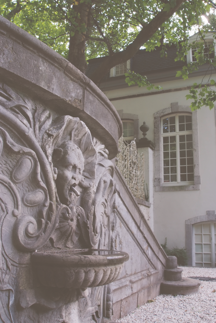 Im Vordergrund ist eine verzierte Stützmauer zu sehen. Im Hintergrund steht der Pavillon auf dem Lousberg.