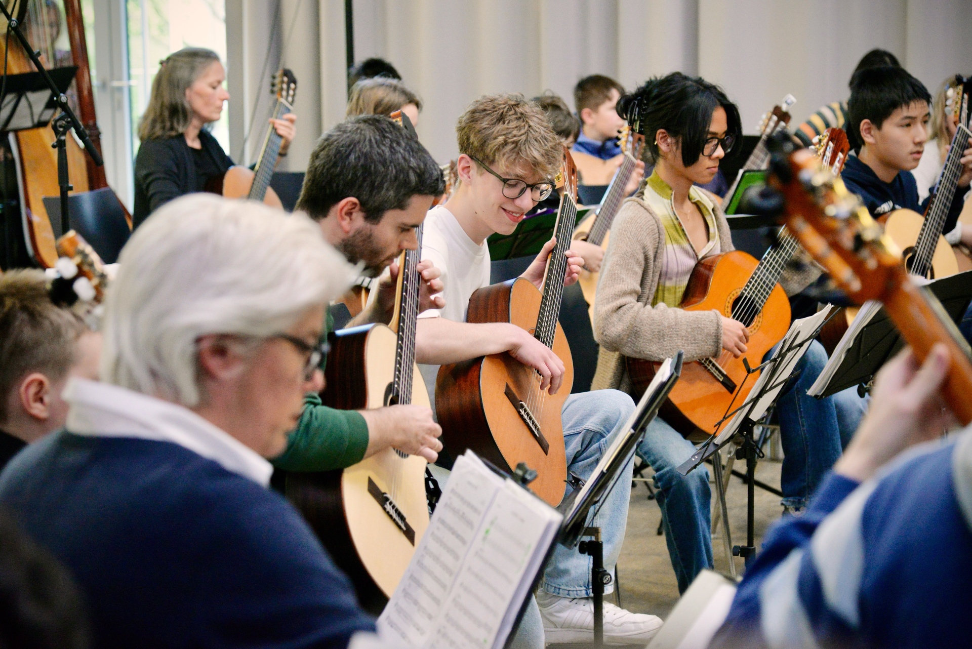 Eine große Gruppe Menschen sitzen vor Notenständern und spielen Gitarre