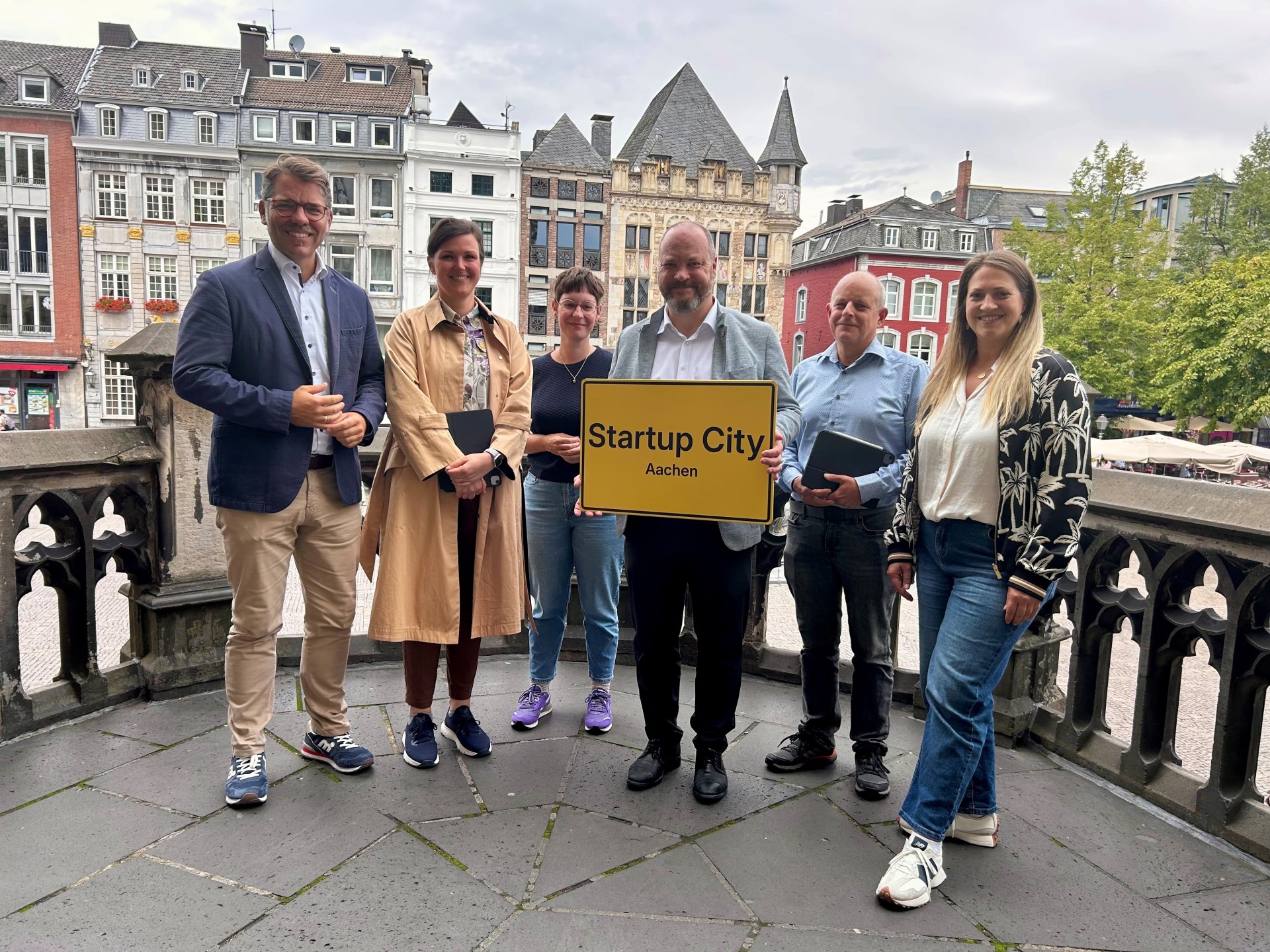 Sechs Menschen stehen nebeneinander. Einer hält ein Schild mit der Aufschrift: Startup-City.